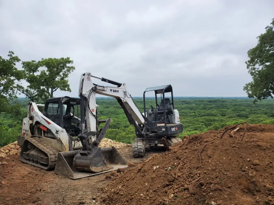 Bobcat skid-steer and mini-excavator on a cleared ridge in North Texas with wide tree-canopy horizon